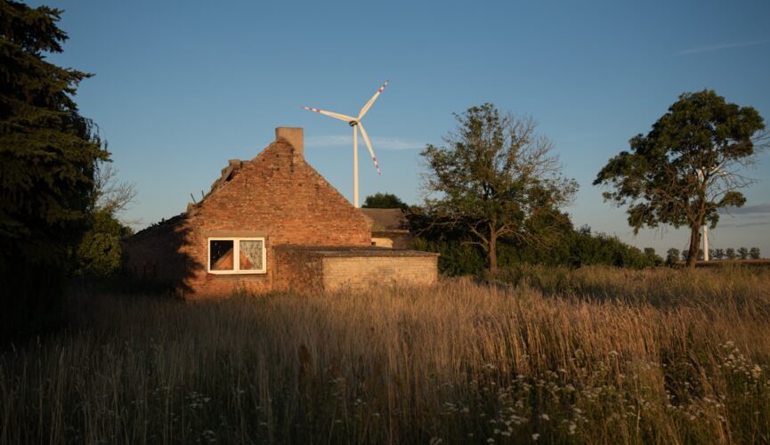Old brick house, wind turbine, and dry field at sunset.