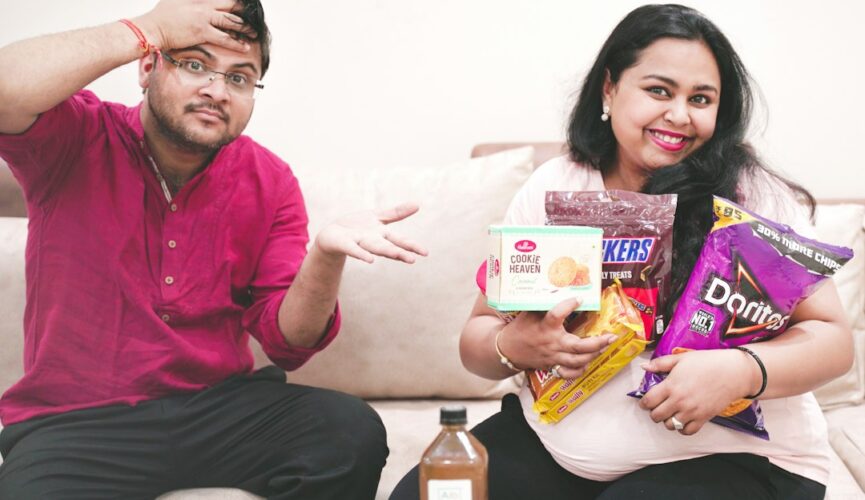 a man and woman sitting on a couch and holding boxes of food